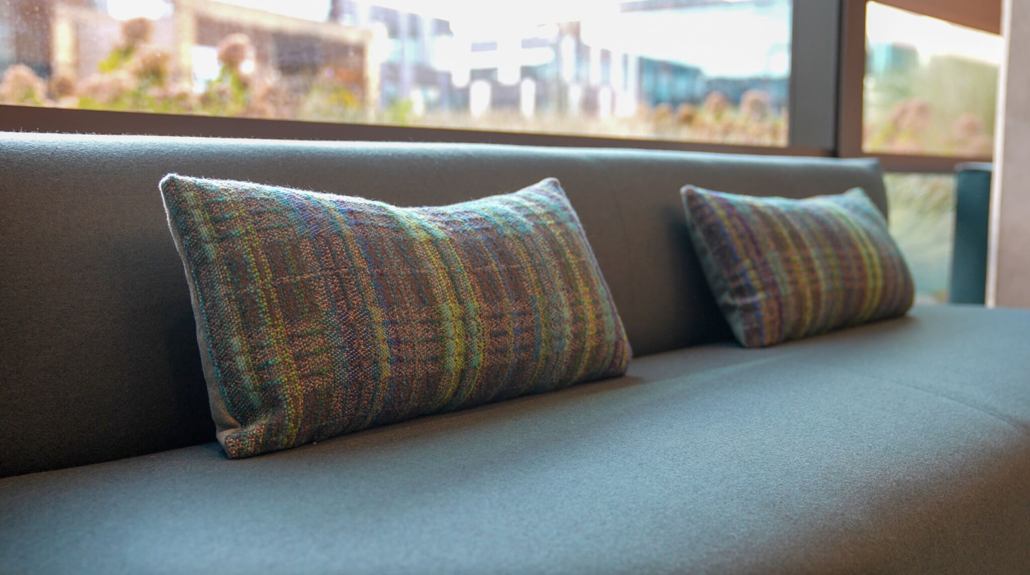Two long lumbar cushion covers in woven multicolor textile on a bench by a window