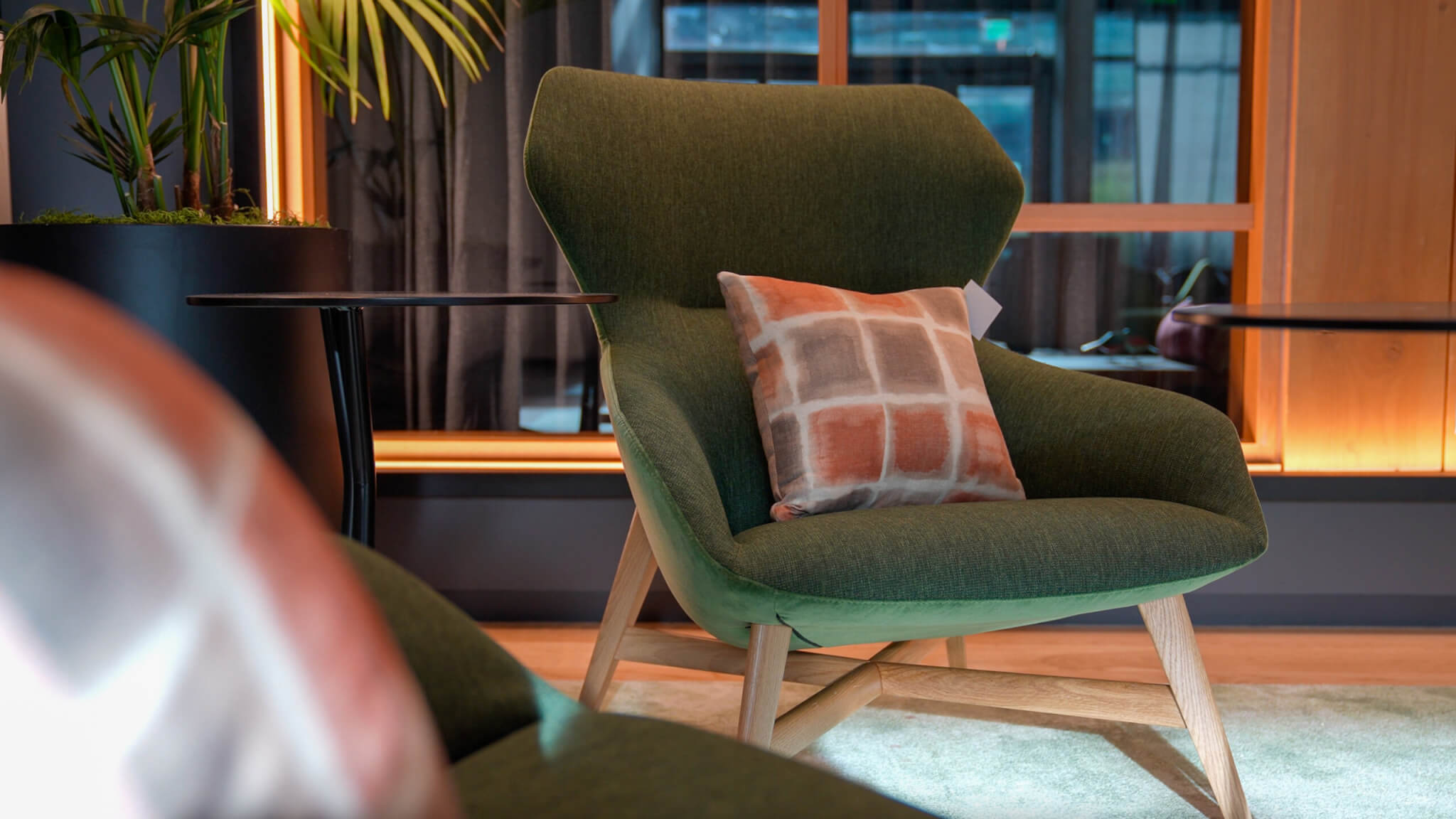 A cushion cover with a watercolor grid pattern in rust and gray on a green lounge chair