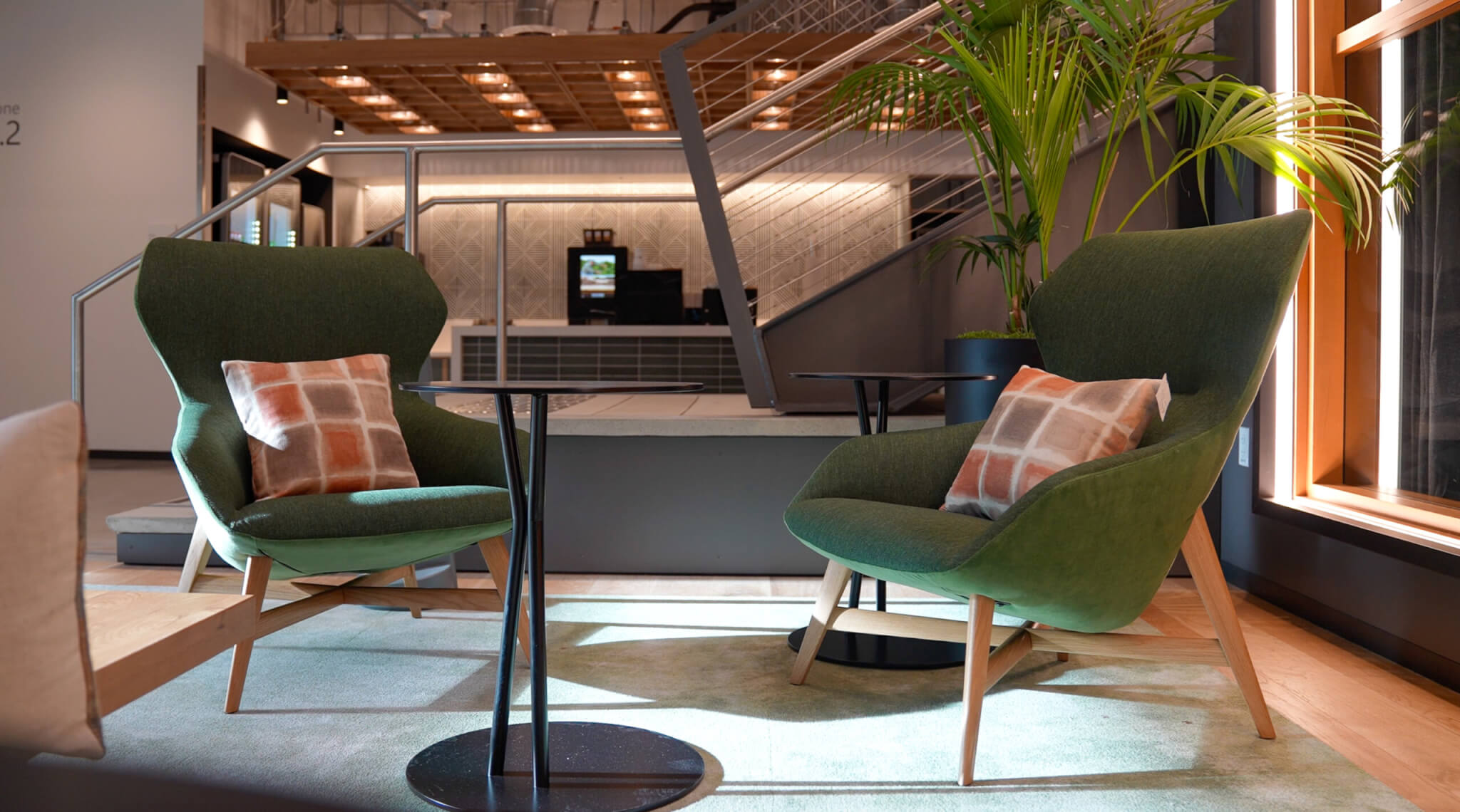Two green lounge chairs with cushion covers beside small round tables in a lobby